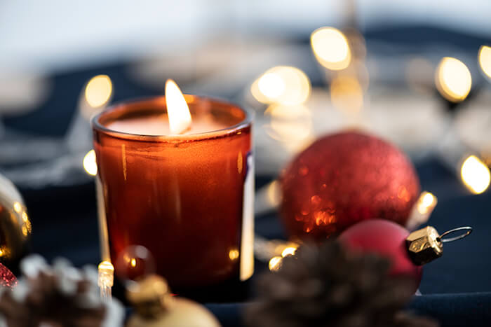 A candle lit next to holiday ornaments.